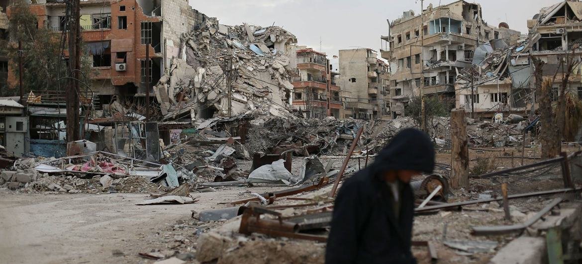 Um homem caminha em frente a edifícios destruídos em Harasta, Síria